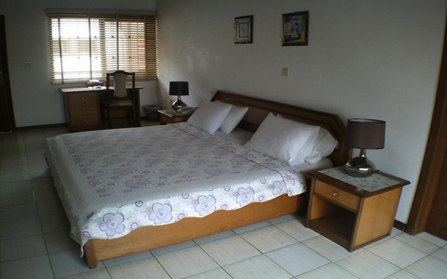 A bright hotel room with a neatly laid mattress and pillows, a cozy bedroom chair, and a table positioned next to a window with natural light streaming in.