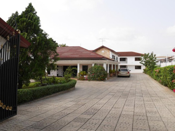 The elegant entrance of a 12-bedroom hotel in the prestigious Airport Residential Area, featuring a contemporary design, a covered walkway, and lush greenery, with plans for future expansion